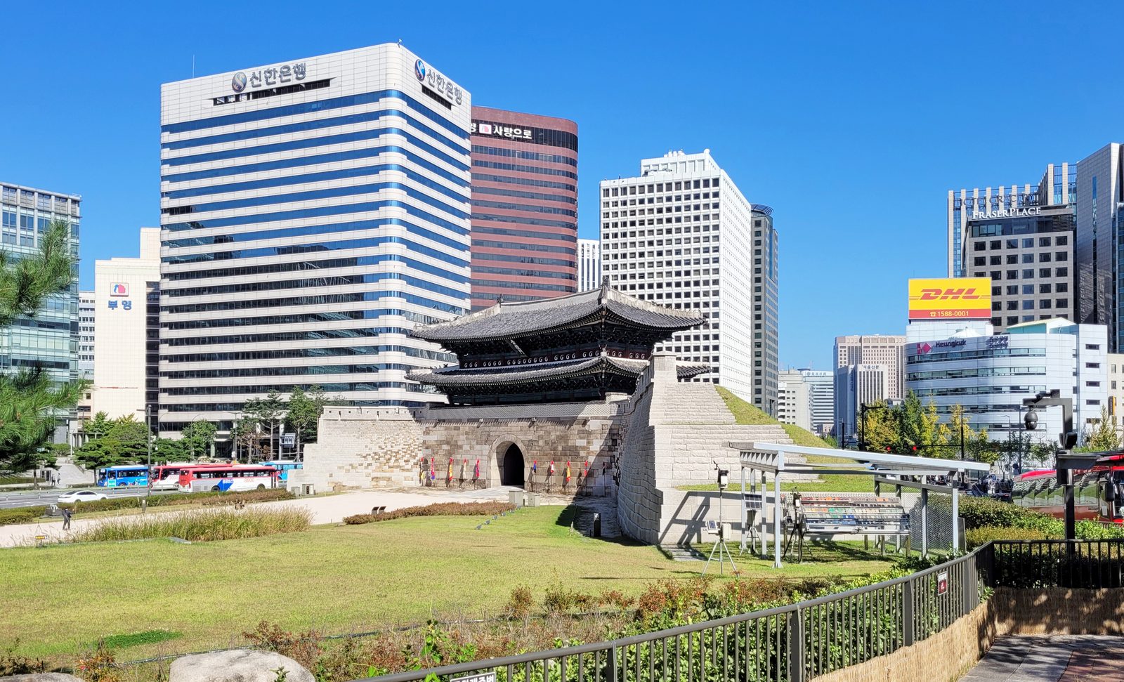 잔디밭 너머에 기와지붕을 얹은 성문이 있어요. 뒤로는 높은 건물이 줄지어 서 있어요.