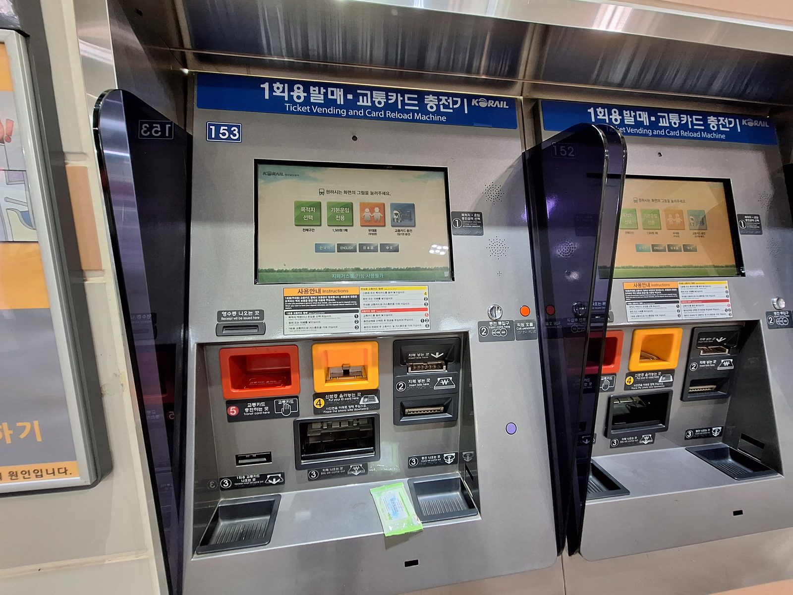 벽에 붙은 큰 기계 두 대예요. 가운데 화면에 그림 단추 네 개가 떠 있고 아래에 카드 넣는 곳이 있어요.