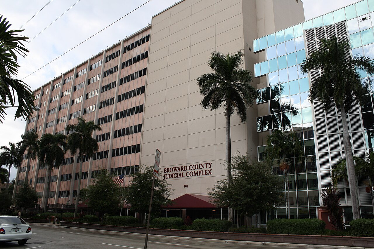 야자수 사이로 보이는 여러 층짜리 건물, 벽에 BROWARD COUNTY JUDICIAL COMPLEX라는 글자가 붙어 있다